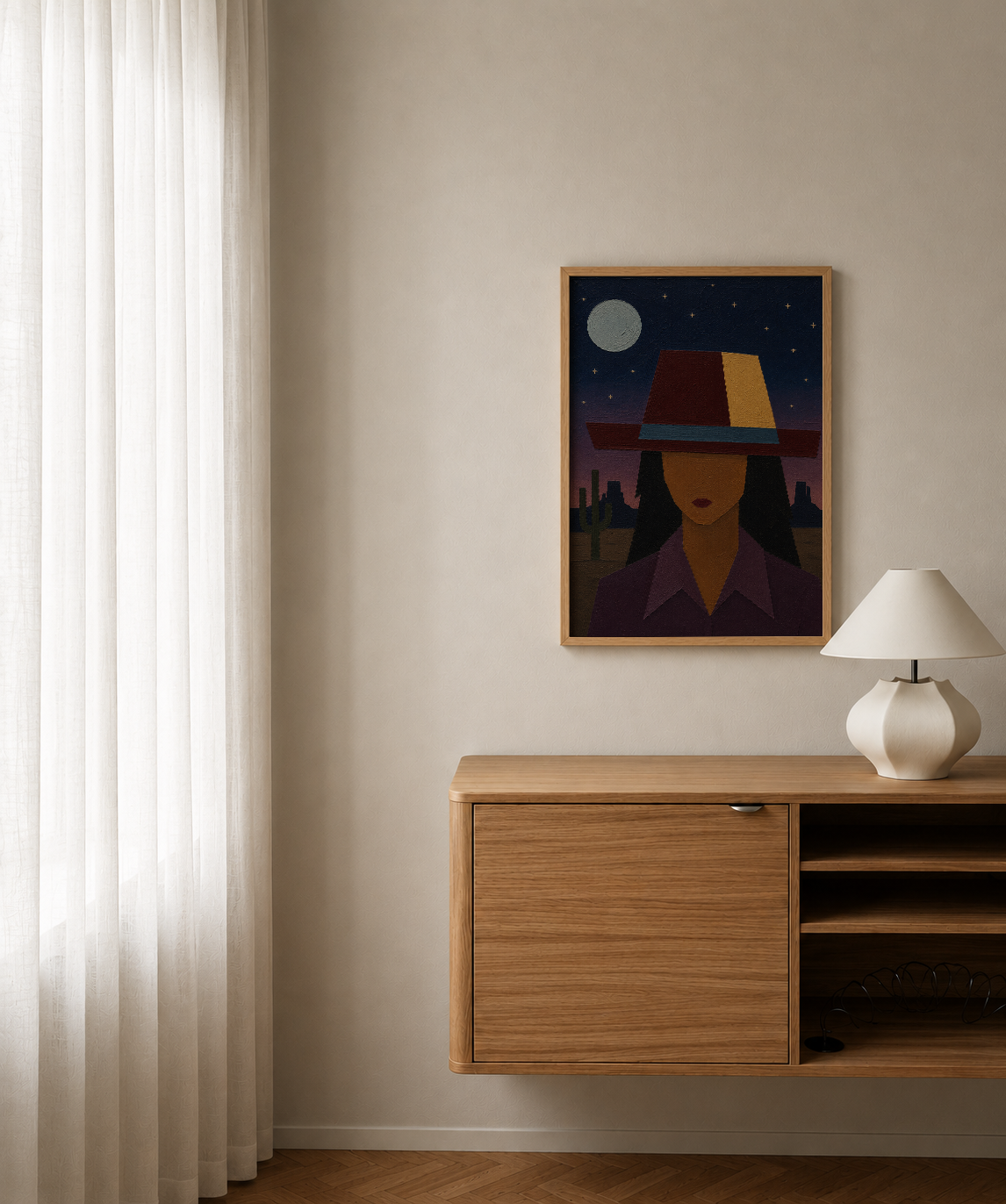 A framed art print featuring a stylized illustration of a woman in a hat under a full moon, displayed on a beige wall above a wooden console table with a white lamp.