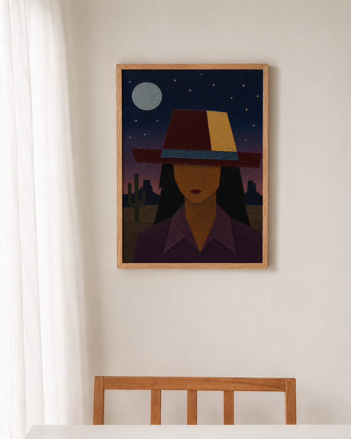 A framed art print depicting a stylized woman in a cowboy hat under a starry night sky, hanging on a light beige wall above a wooden chair.