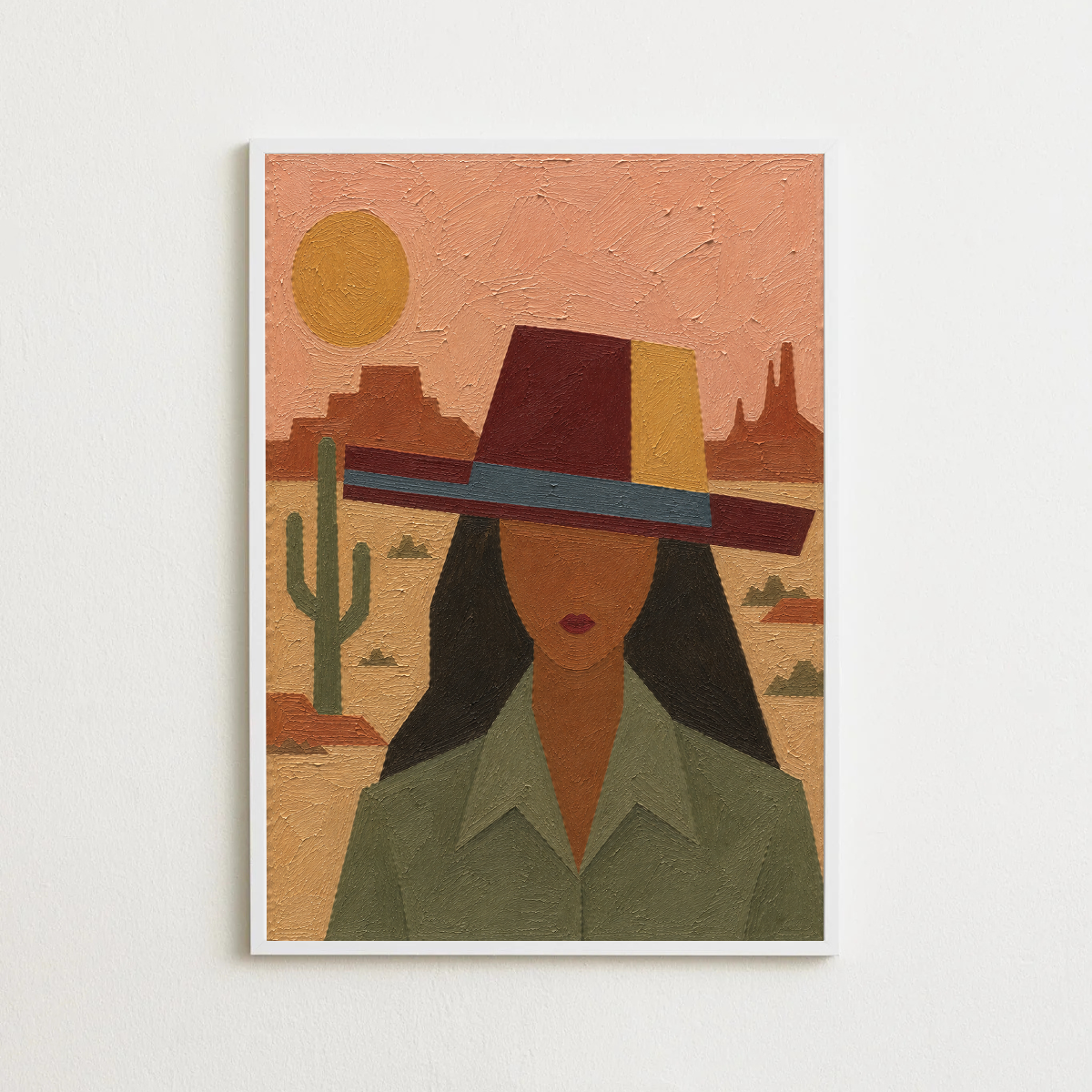 A framed art print featuring a stylized desert portrait of a woman wearing a wide-brimmed hat, displayed on a light off-white wall.