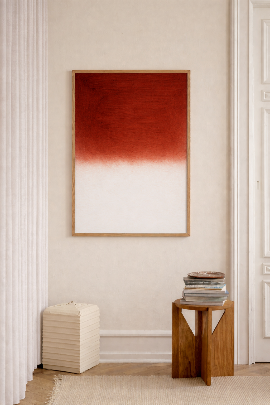 Abstract art piece with red and white gradient on a beige wall, with a wooden side table and white ottoman below.